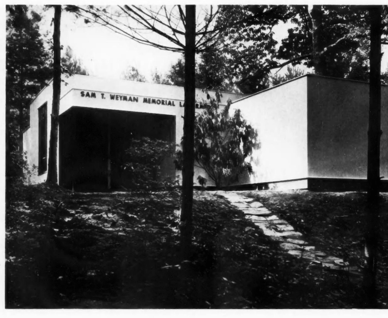 Masa's photograph of the Weyman Laboratory entrance, its lettered fascia reading SAM T. WEYMAN MEMORIAL LABORATORY, seen through bare trunks with a stone path leading up.