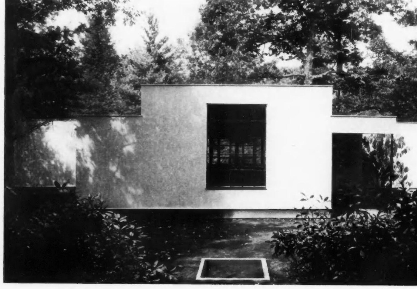 Masa's photograph of a flat white elevation of the Weyman Laboratory with a single large window and rhododendron in the foreground.